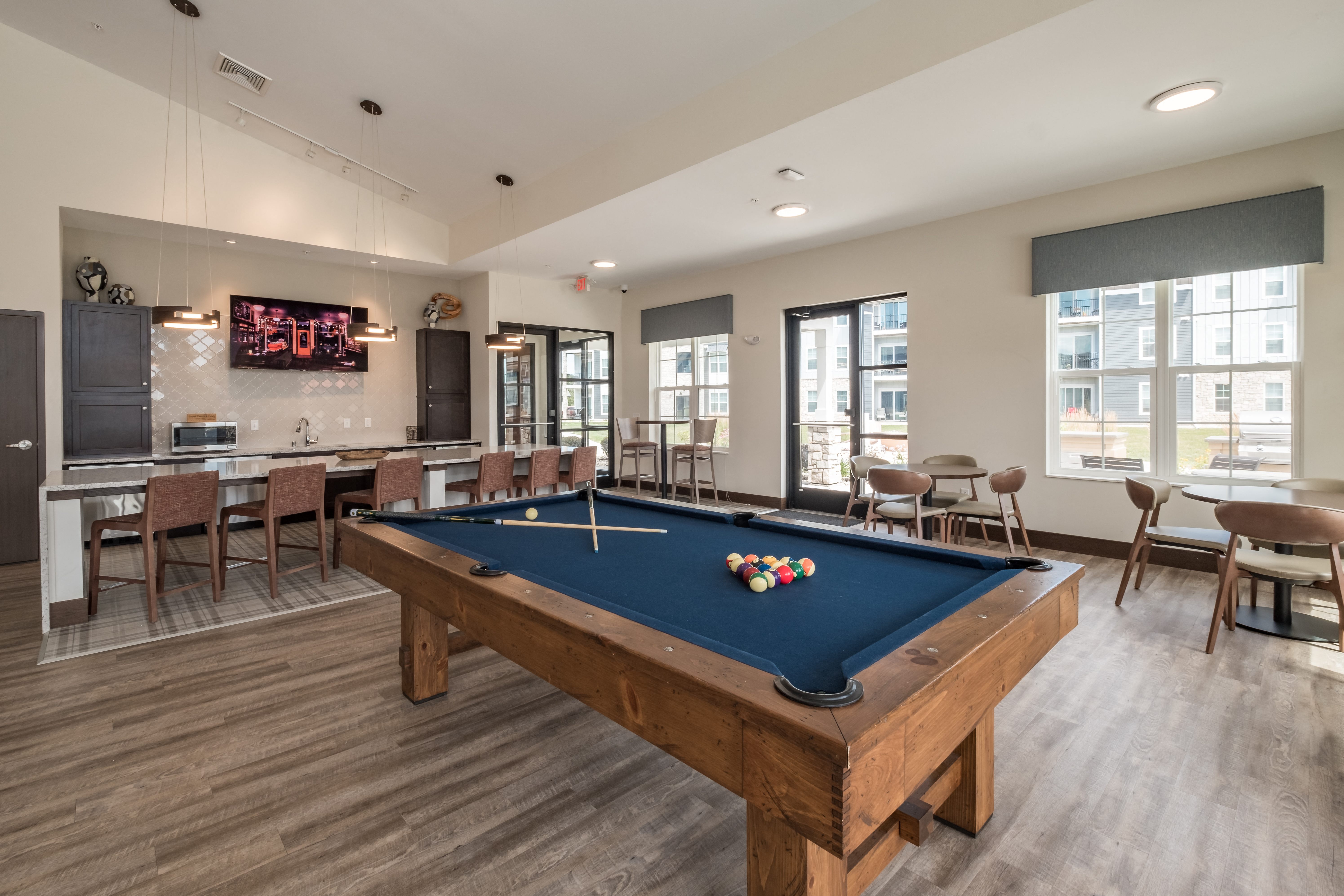A pool table is in the middle of a room with a bar and chairs.